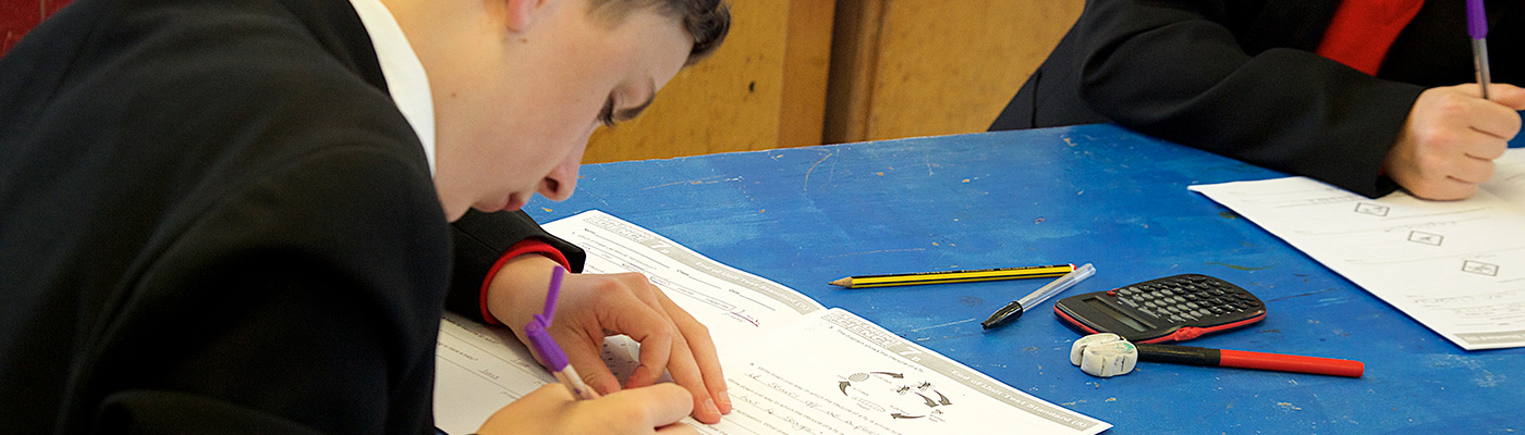 Male school student writing on paper in classroom