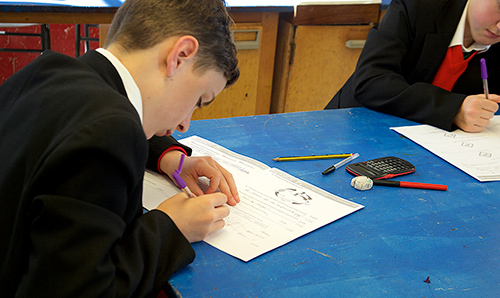 Male school student writing on paper in classroom