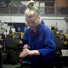 Student in blue lab coat working on machine in workshop