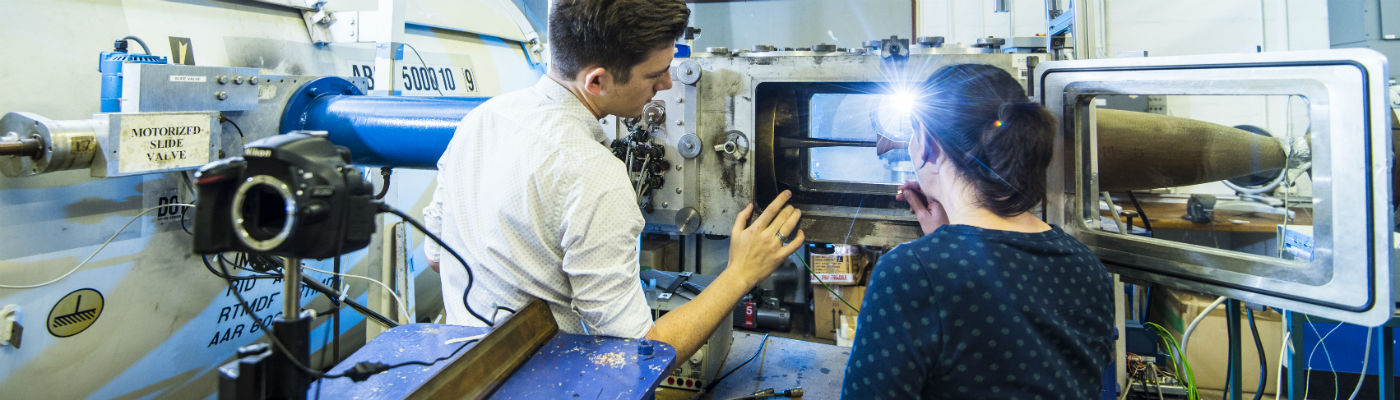 Two students, backs to camera, in front of open machine, discussing its contents