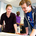 Professor and student leaning over a worktop while smiling
